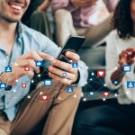 stock_photo_of_two_people_smiling_and_looking_at_cell_phones_with_social_media_like_and_heart_buttons_appearing_to_fly_by