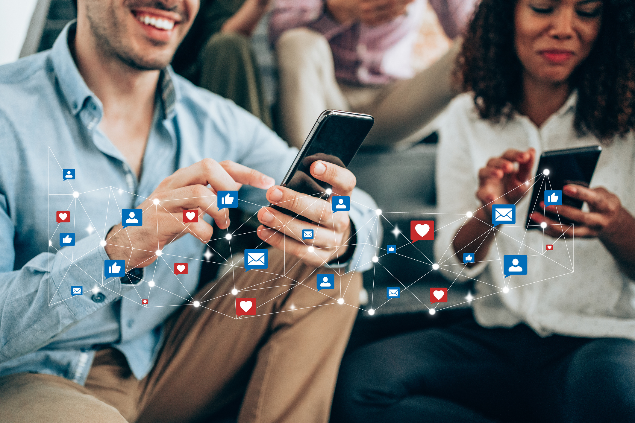 stock_photo_of_two_people_smiling_and_looking_at_cell_phones_with_social_media_like_and_heart_buttons_appearing_to_fly_by